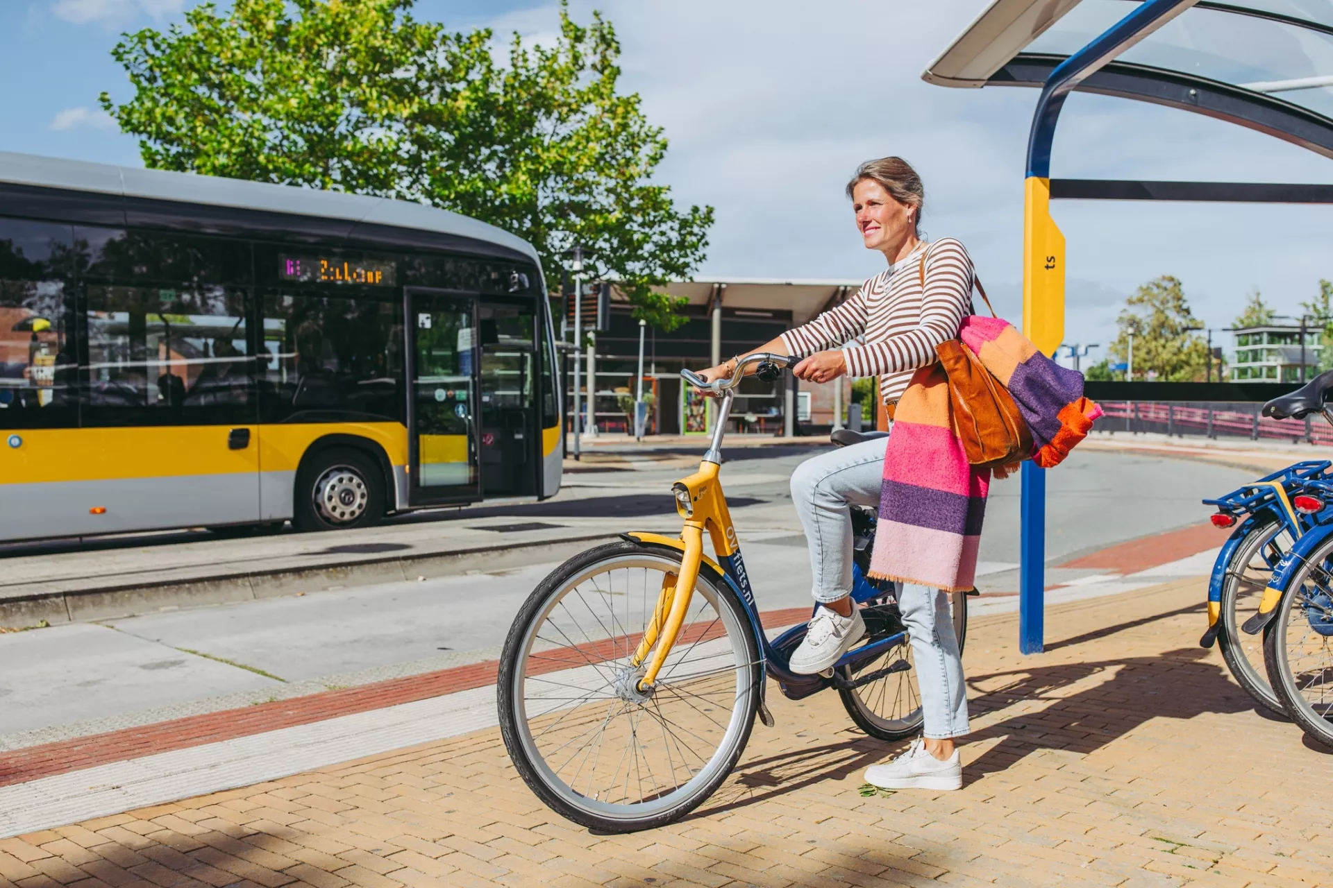 Vrouw op fiets bij bushalte op zonnige dag.